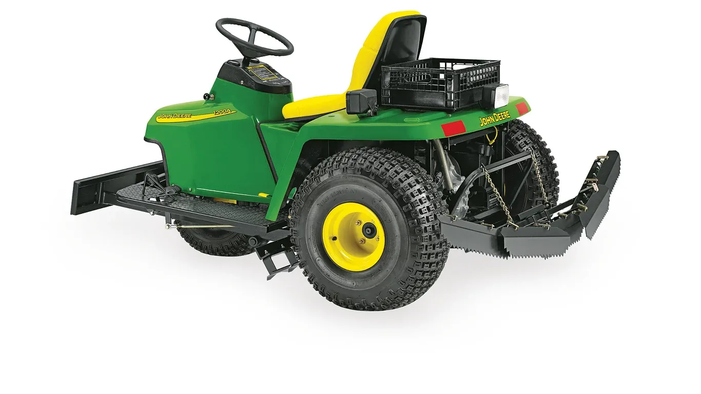 Bunker rake in green and yellow with rear grooming attachment, wide turf tires and operator seat for golf course bunker maintenance