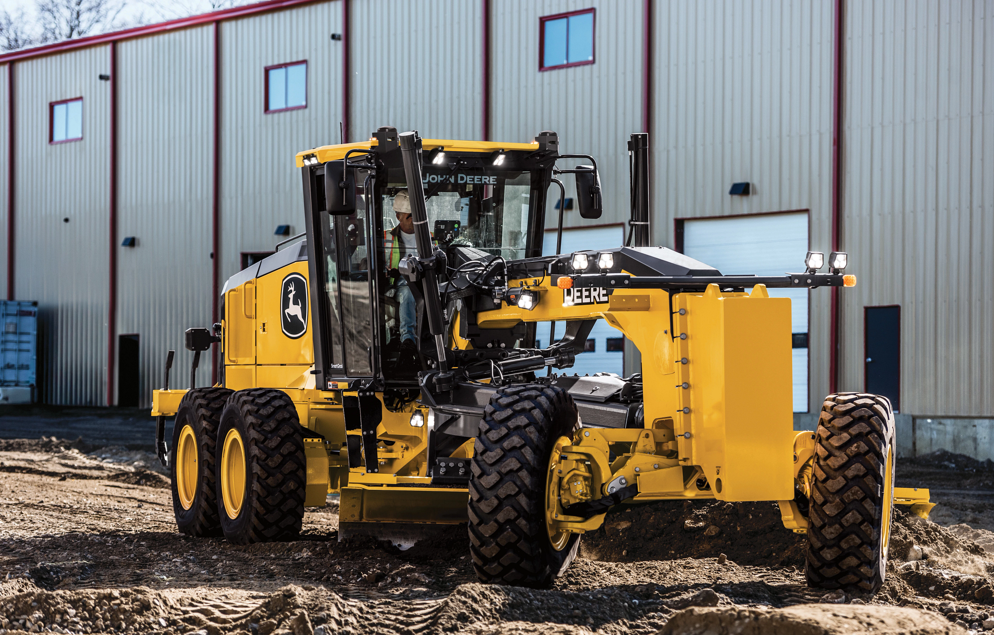 Front right view of an 872P Motor Grader on a dirt lot in front of a warehouse
