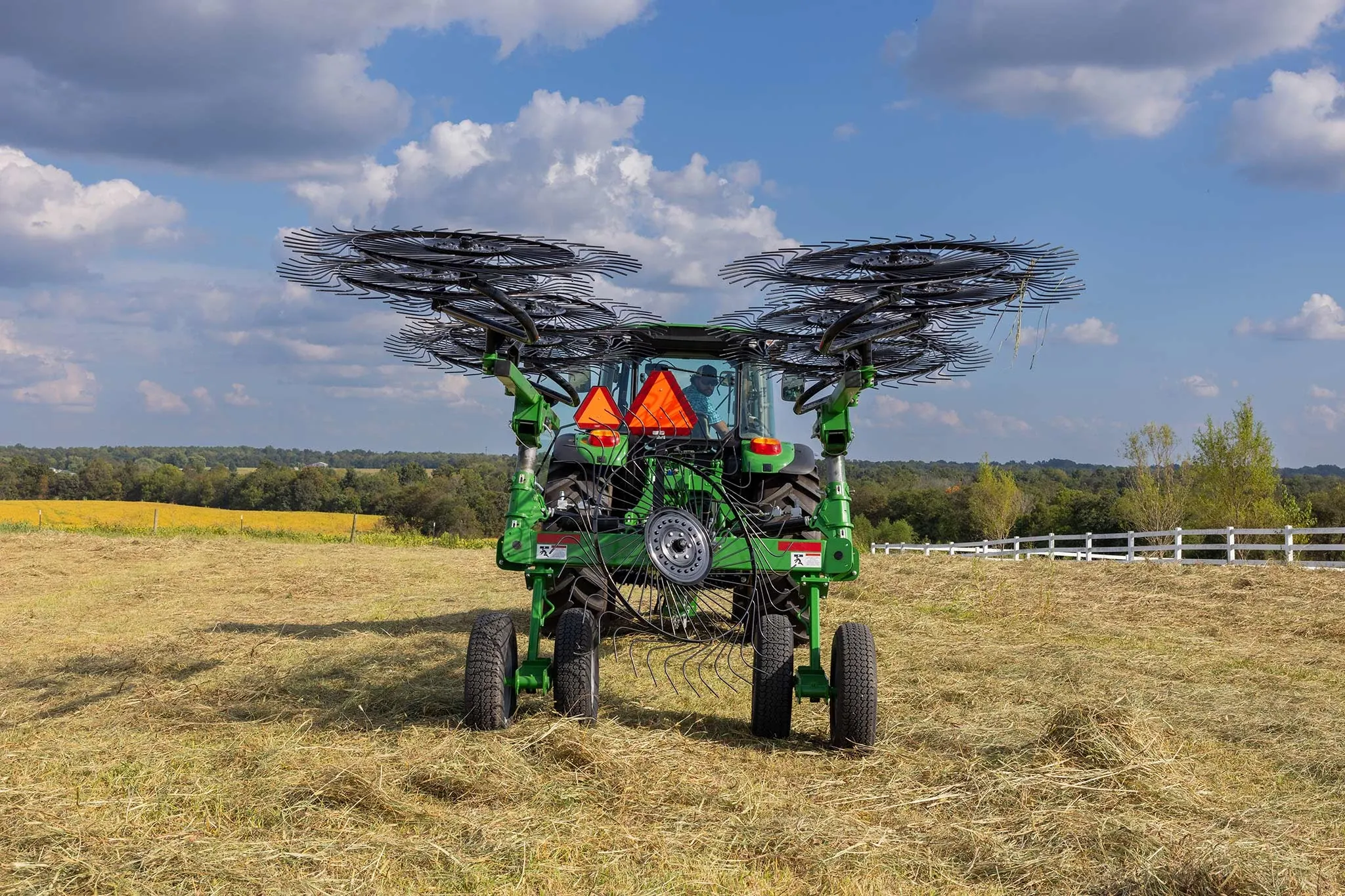 Rear view of a 5125M tractor in a hay field with WR3210 wheel rake folded into transport mode