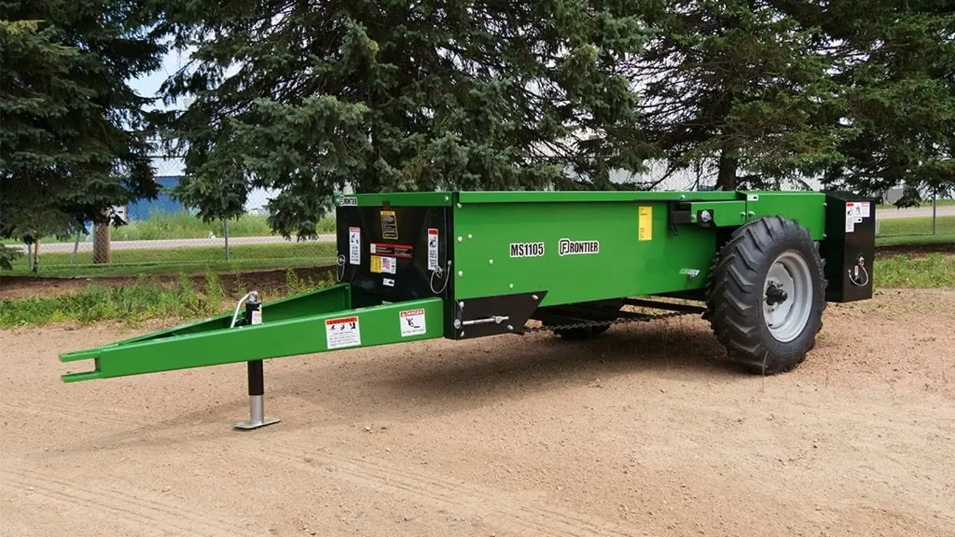 Front left of MS11G Series Small Manure Spreader sitting in dirt besides trees