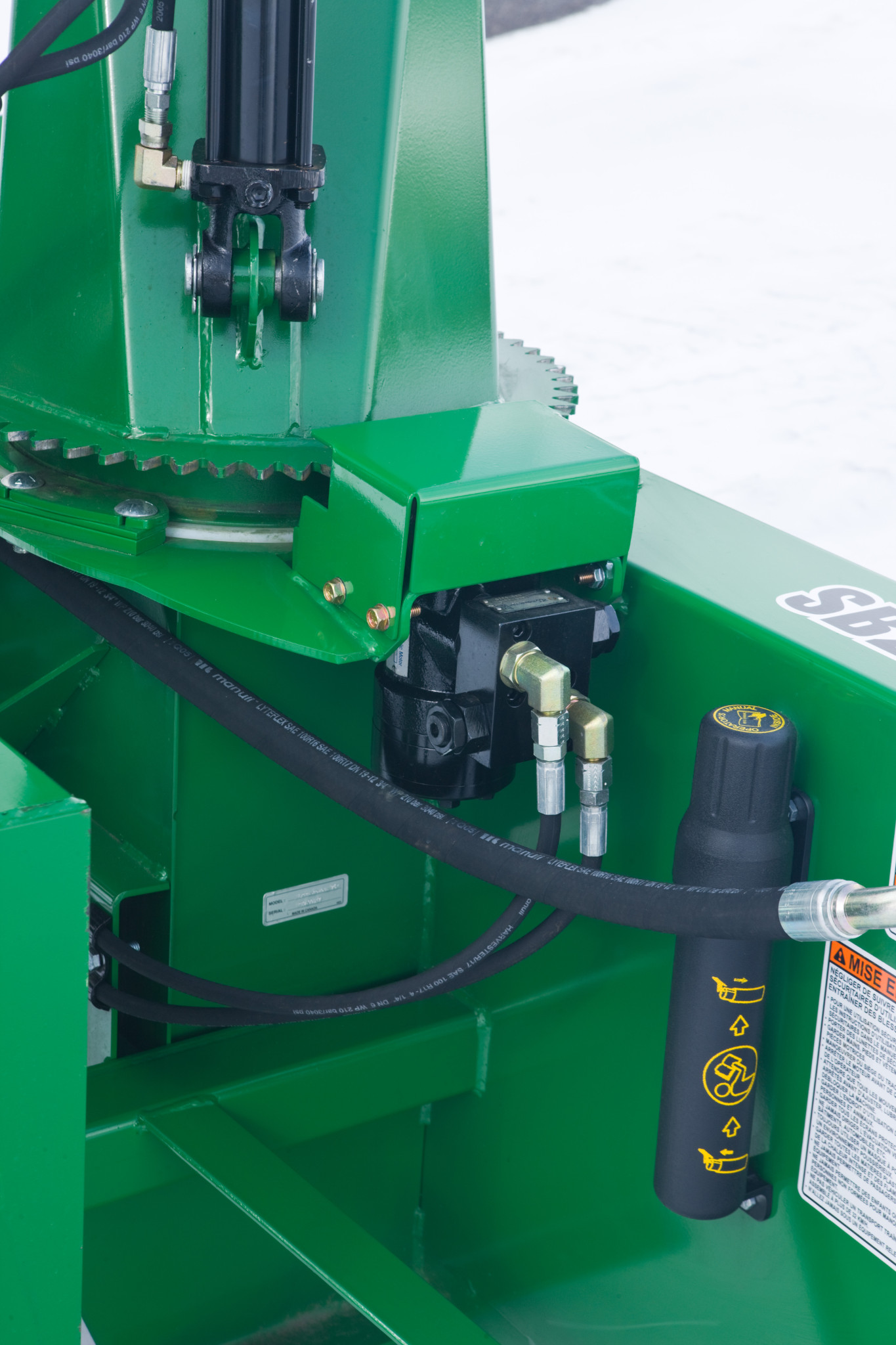 Close-up of a snowblower showing hydraulic hoses and fittings connected to a toothed rotation gear