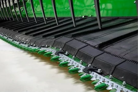 A close-up view of a green draper platform showing the row of serrated sickle sections and black belts above them