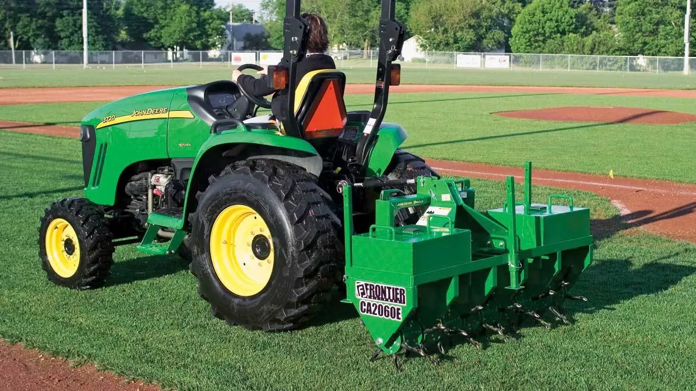 Tractor pulling a CA2060E Core Aerator on the third base side of a baseball field