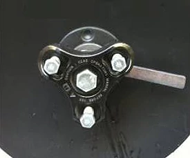 Close-up of a mechanical metal gang bolt with a black triangular plate, three silver hex bolts, a central hex nut, and a metal lever extending to the right