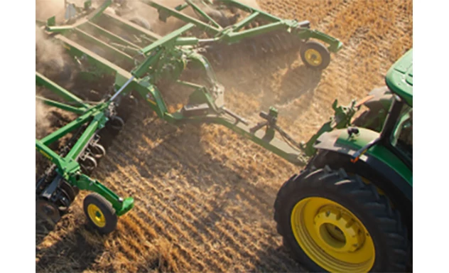 Green tillage implement with a front hitch and hydraulic lines, showing angled disc blades arranged in rows behind the frame