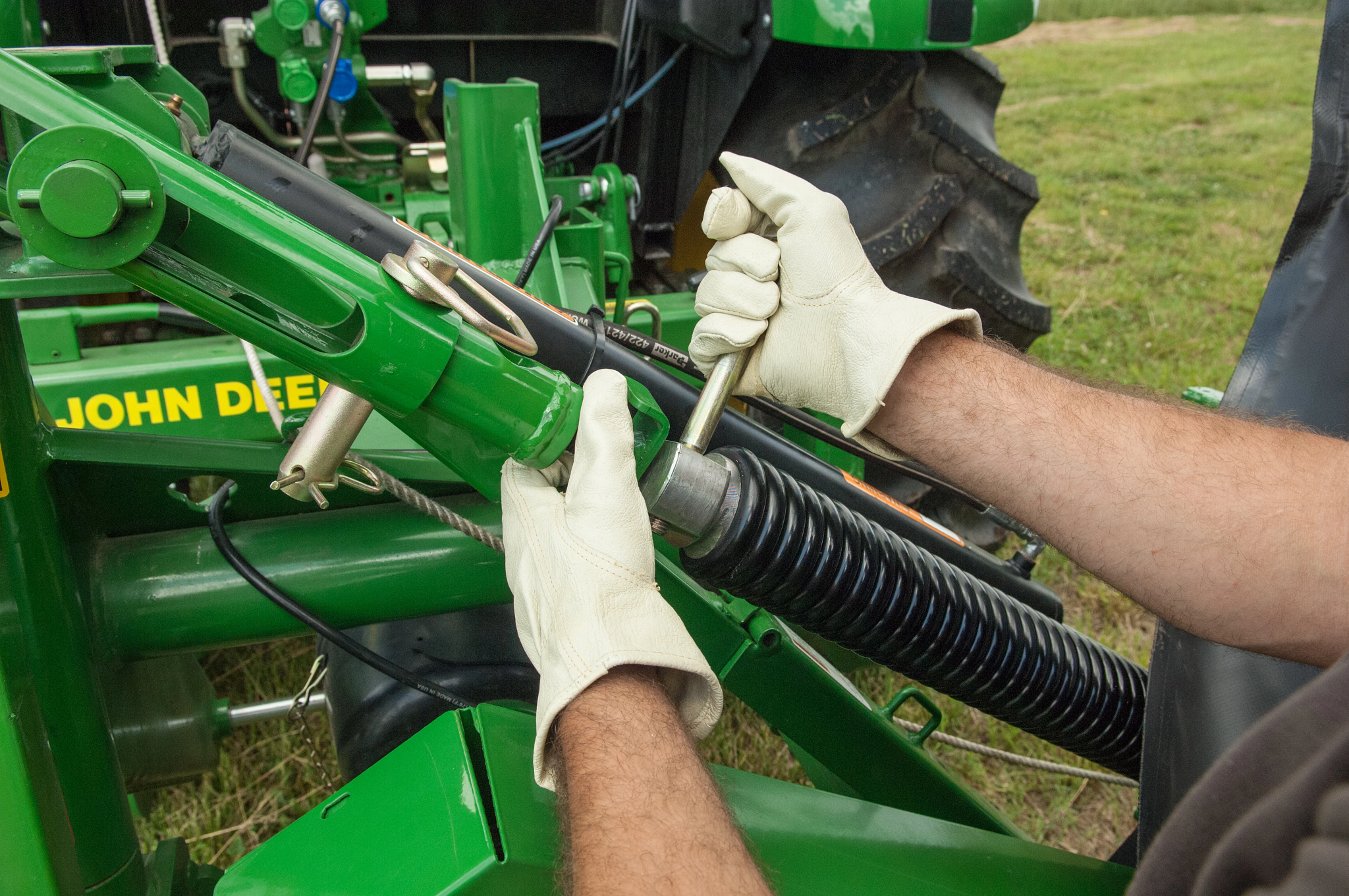 Two gloved arms adjusting the float spring on a DM5060 Disc Mower