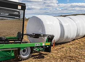 Side left view down a line of white plastic-wrapped round bales being pushed by an LW1166 inline bale wrapper in a harvested field