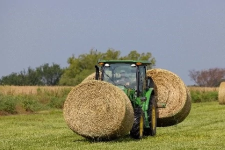 A tractor in a field transporting three large round hay bales, with one bale carried on the front and two positioned behind the tractor