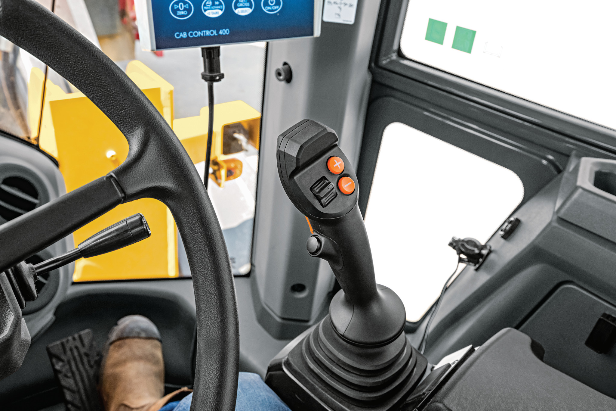 Interior view of wheel loader cab showing a steering wheel and a control joystick with orange buttons mounted on a black base