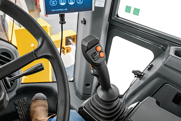 Interior view of wheel loader cab showing a steering wheel and a control joystick with orange buttons mounted on a black base