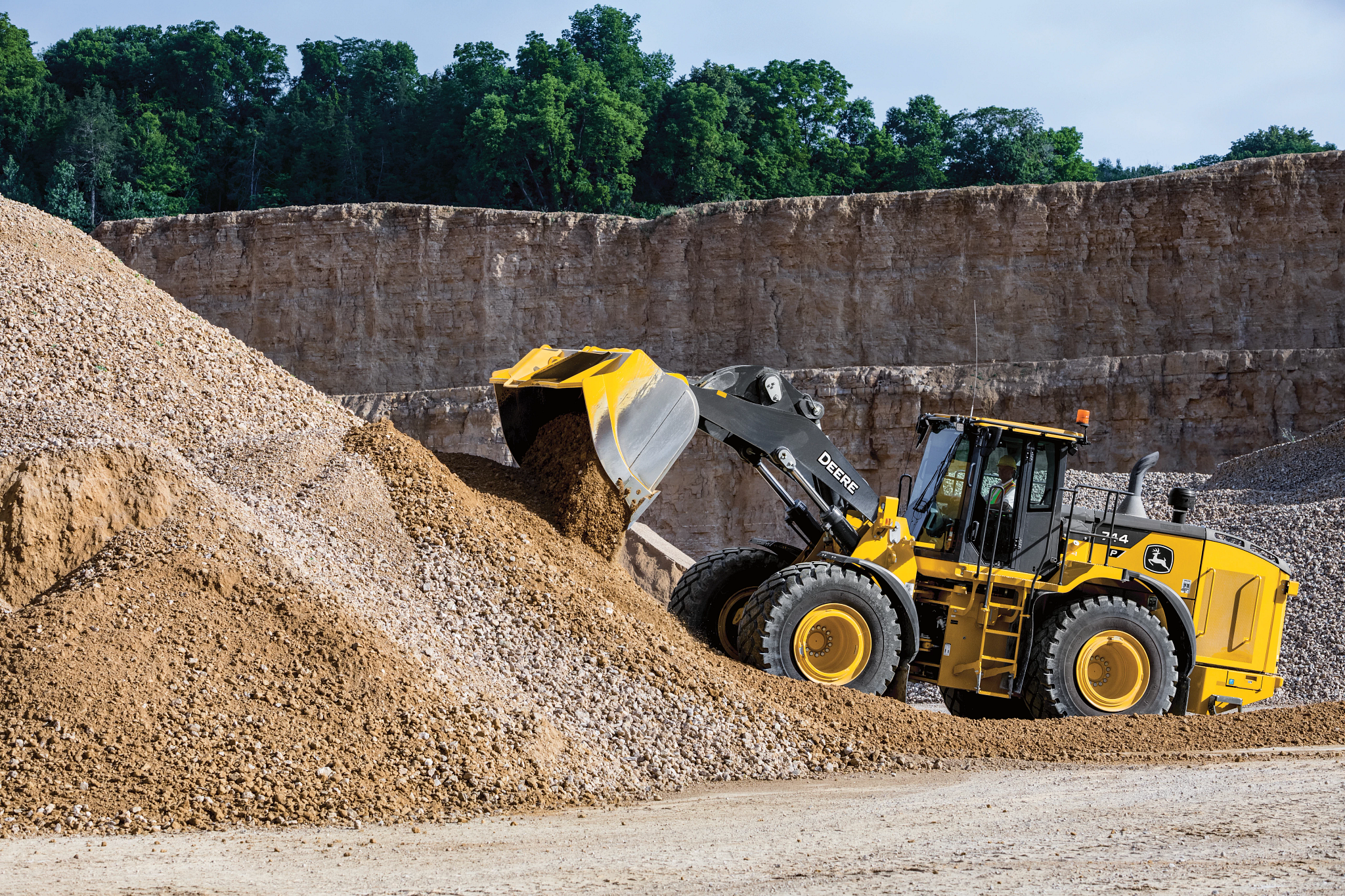 A large yellow front-end loader scoops and lifts gravel from a steep pile in a quarry