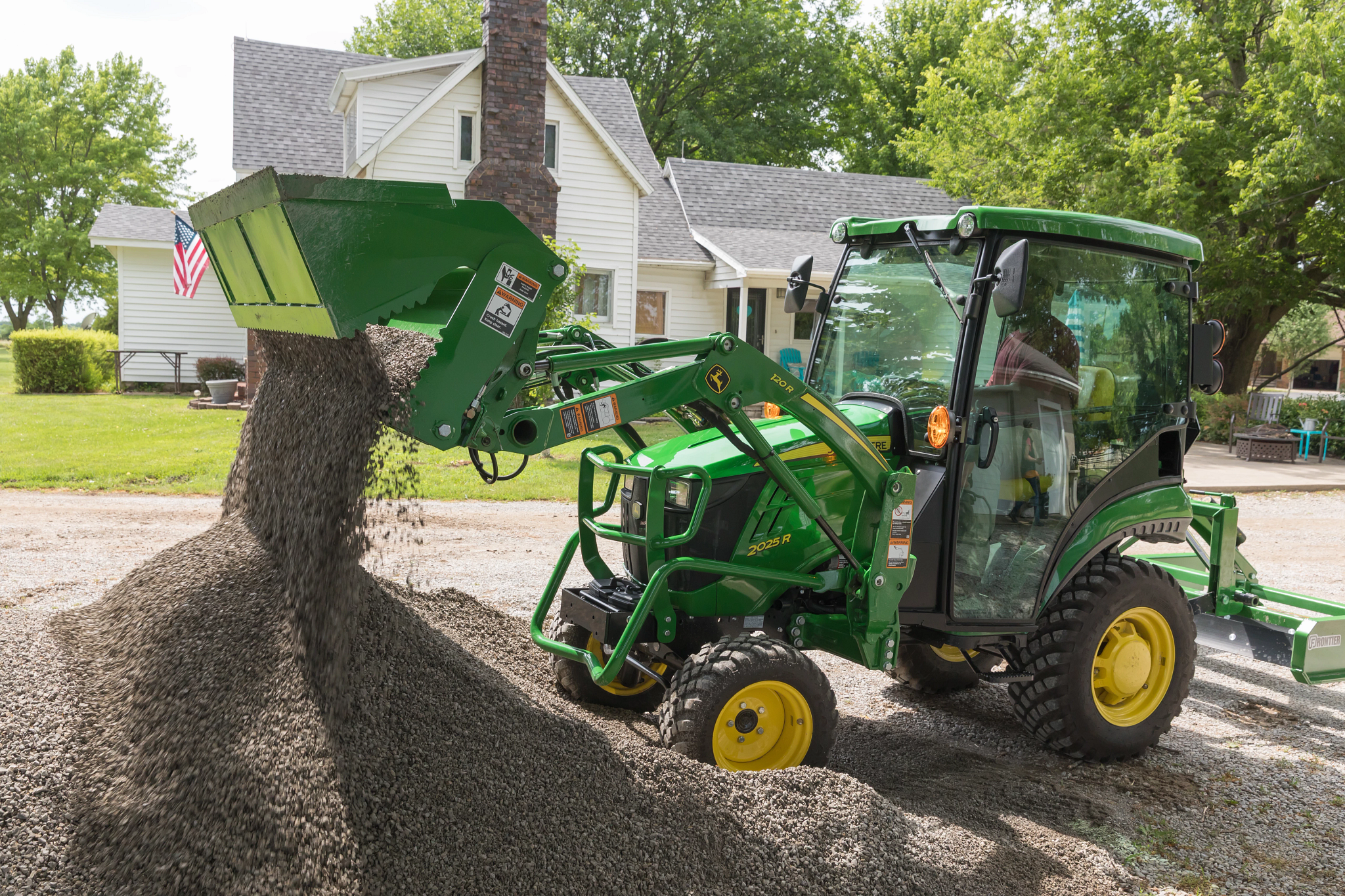 Side left view of a 2025R tractor with 120R loader and AY11F 4-in-1 bucket dropping gravel in a pile on a residential street