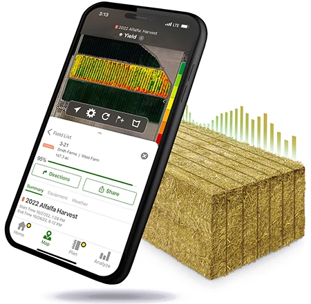 A smartphone displaying a crop‑yield map shown angled in front of a stacked hay bale graphic, illustrating digital farm data analysis