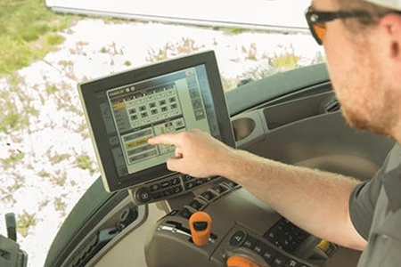 Left, angled view from a farmer's shoulder of his hand pressing a point on a digital TruSet™ display from within a machine's cab