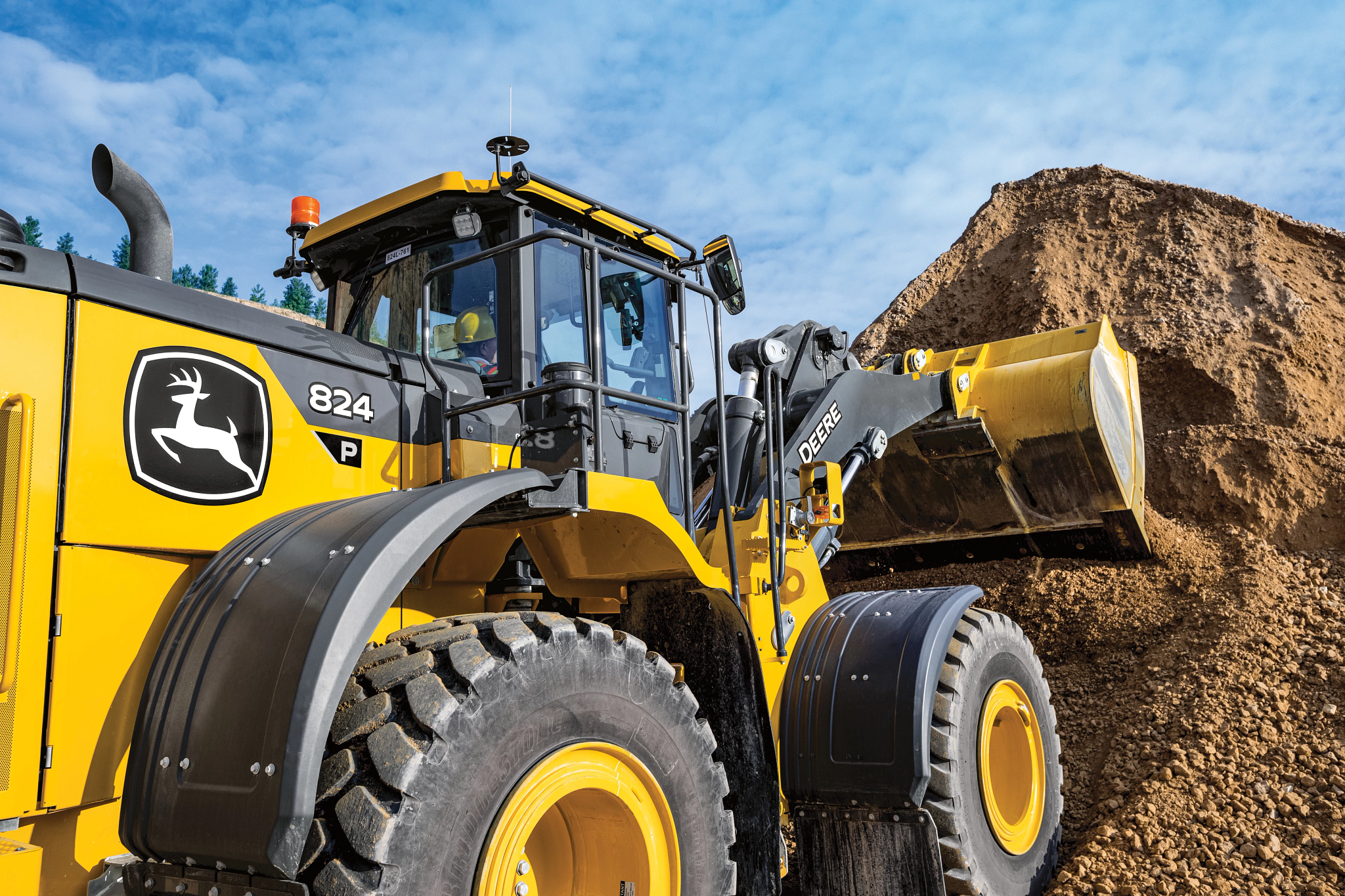 Close-up of a large yellow front-end loader working at a quarry, with its bucket raised and pressed into a tall pile of earth and gravel