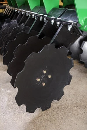 Close-up view of a row of black notched disc blades mounted under a tillage implement, shown from a low angle on a concrete surface