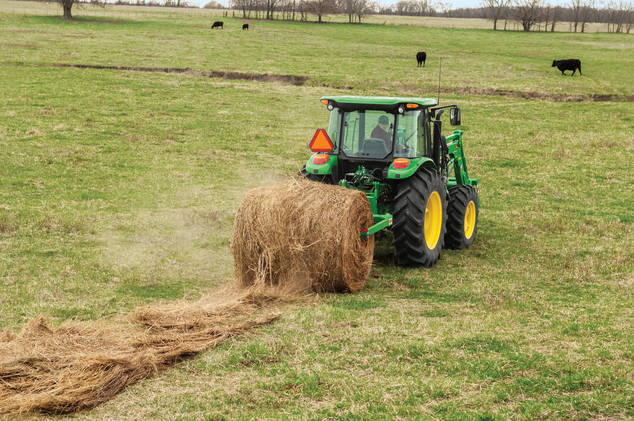 A rear view of a Tractor with a BU1060 Bale Unroller unrolling a hay bale in a field