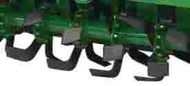 Underside of a green rotary tiller implement showing a row of evenly spaced curved tines used for soil engagement