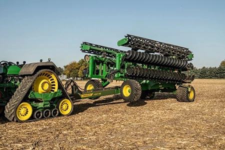 Tracked tractor pulling a folded tillage implement with multiple disc gangs, shown in transport position across a harvested field