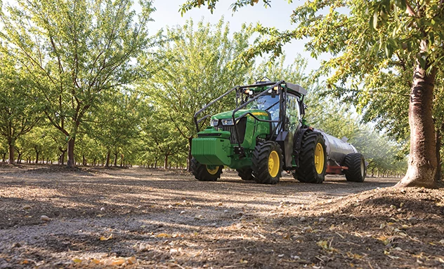 Front left view of a tractor pulling an implement through a fruit orchard