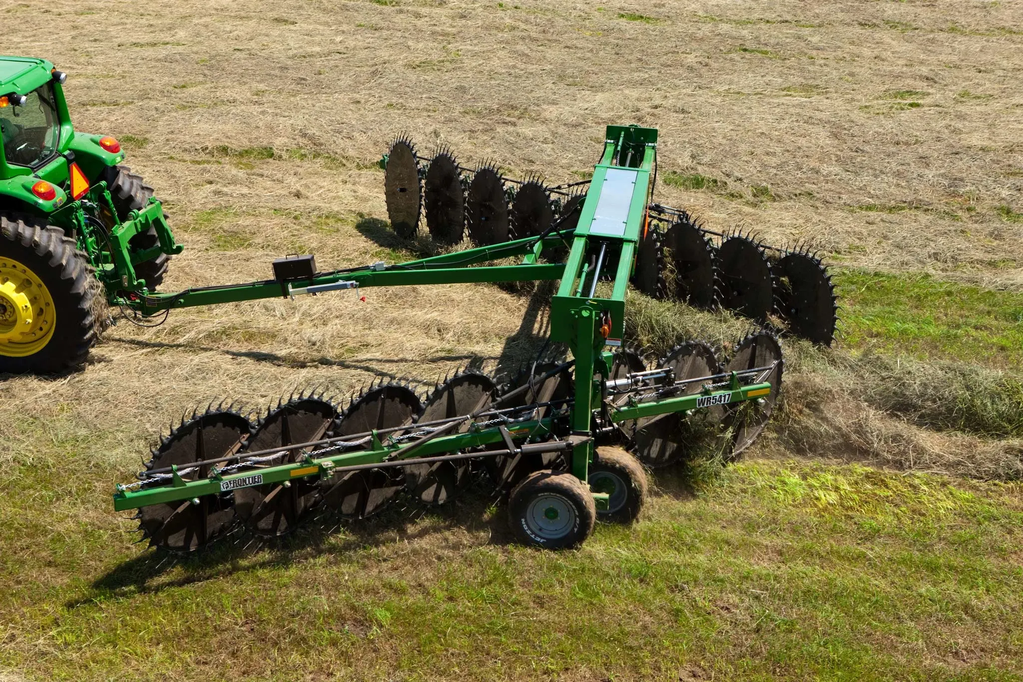 Aerial view of a WR high-capacity wheel rake being pulled across a hay field by a tractor