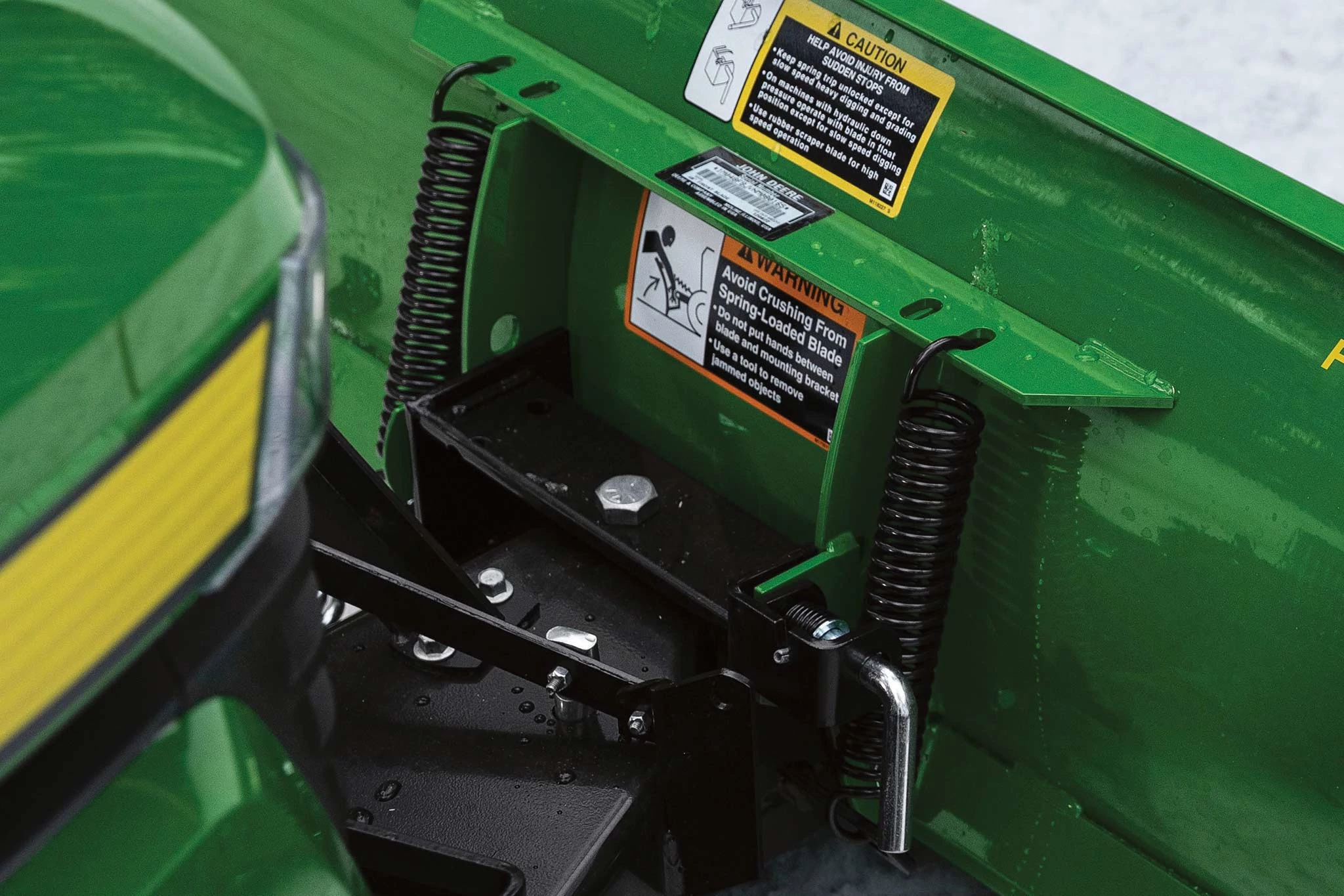 Close-up field image of a green Front Blade's breakaway spring mechanism where connected to a lawn tractor