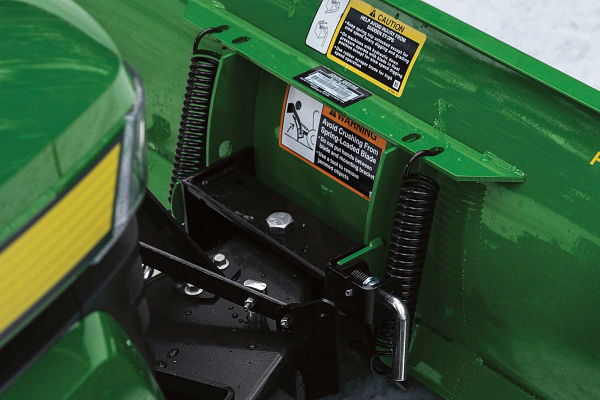 Close-up field image of a green Front Blade's breakaway spring mechanism where connected to a lawn tractor
