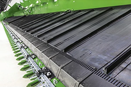A close-up view of a green draper platform showing the row of green cutterbar sections and black belts above the cutting system