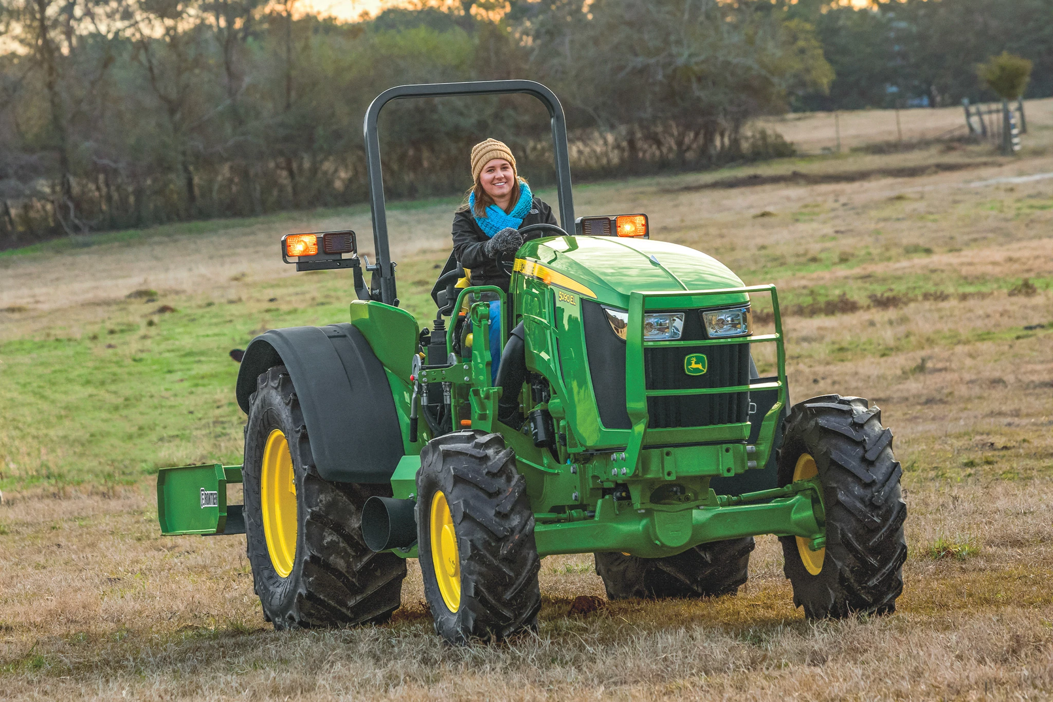Operator driving an open operator station John Deere compact tractor across a pasture