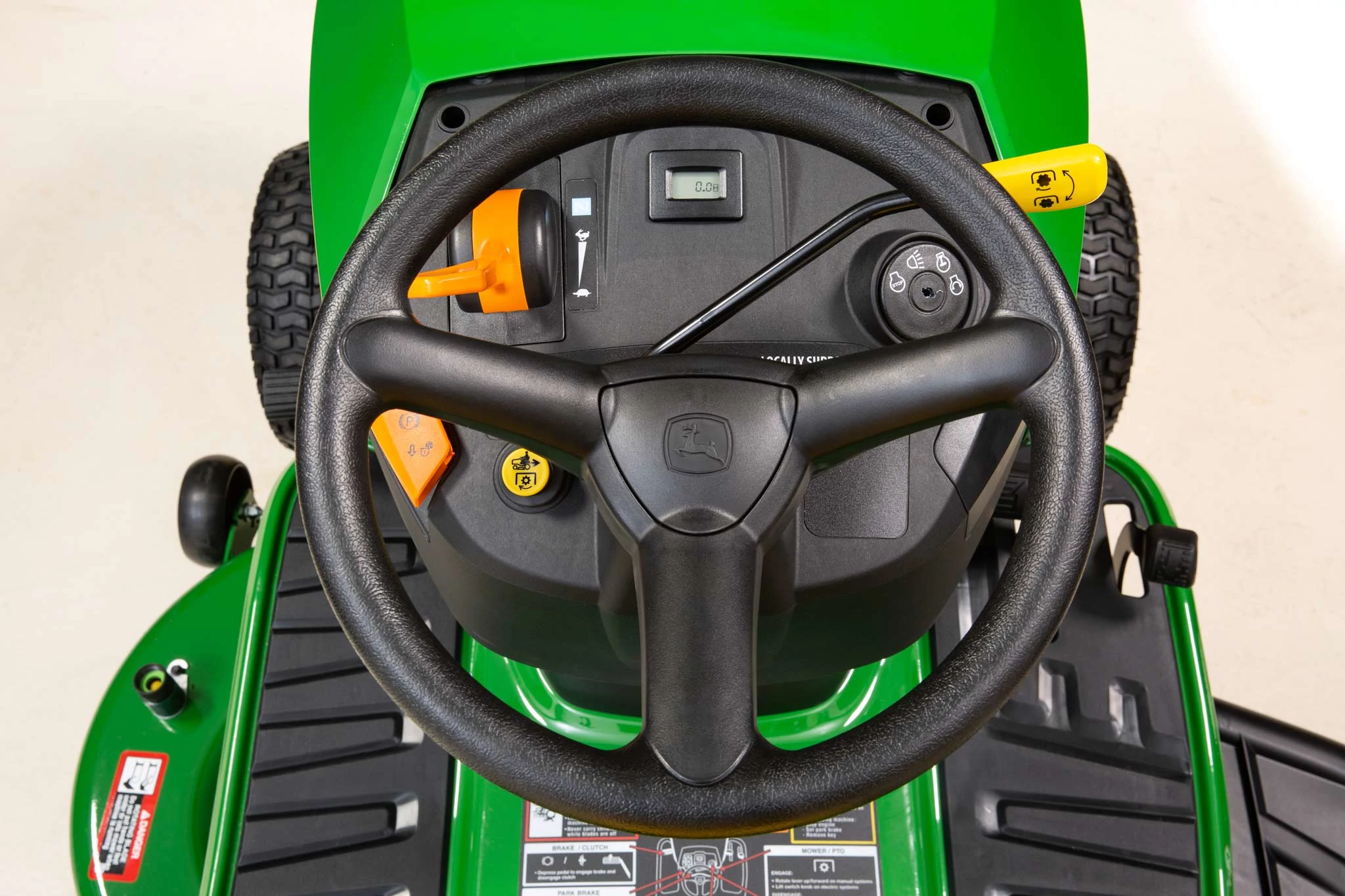 Top studio view of an S110 lawn tractor's steering wheel, dash, and foot pads