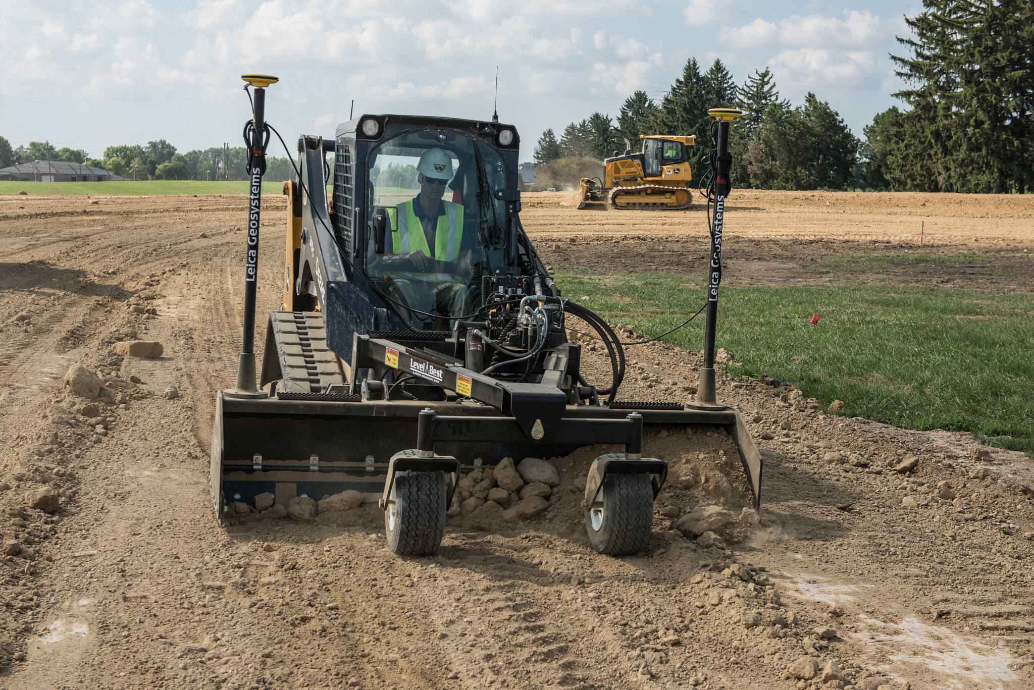 Front view of a 317G Compact Track Loader grading dirt lot with attached front box blade