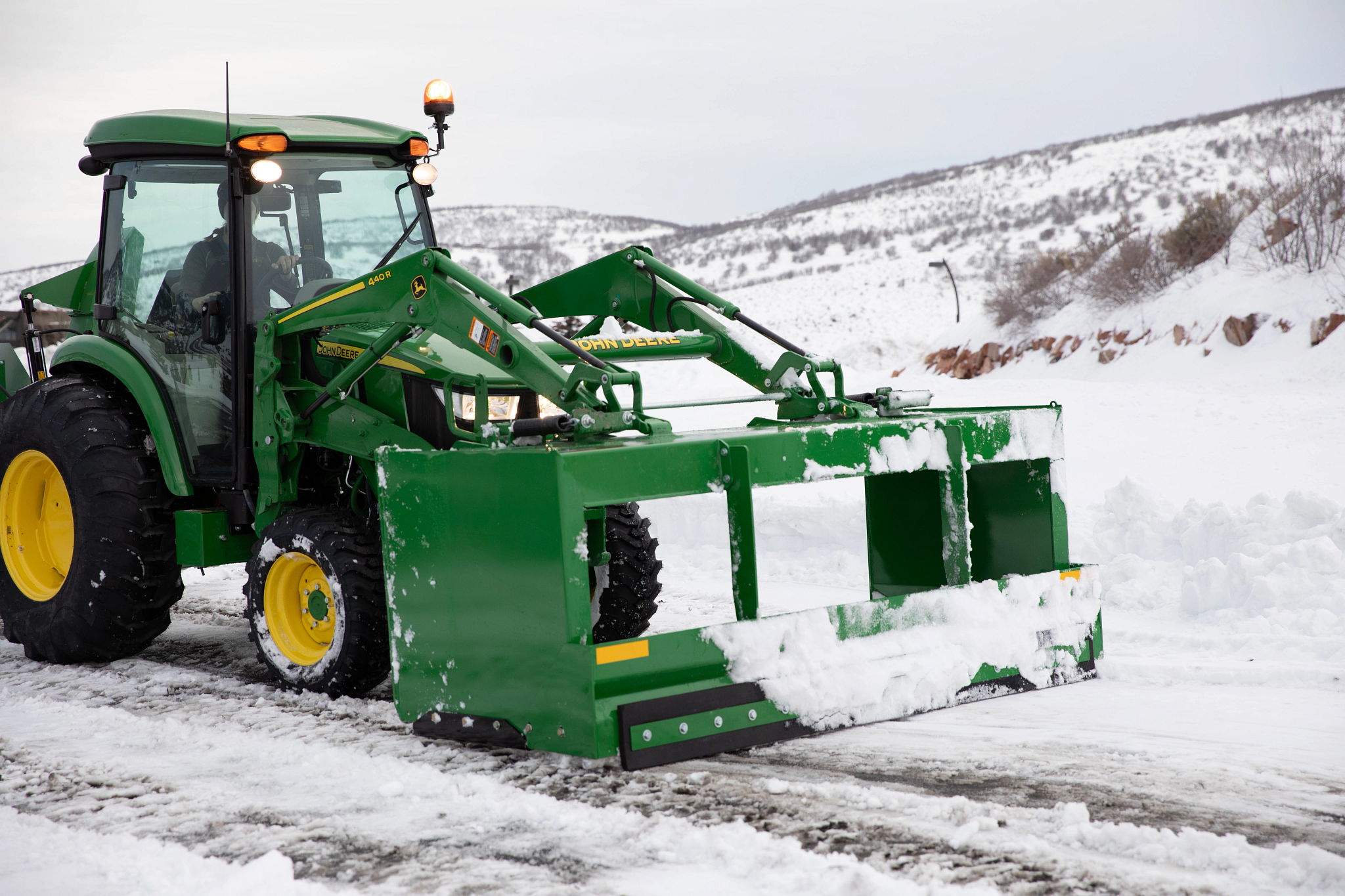 Tractor equipped with a front-mounted snow pusher clearing snow from a road.