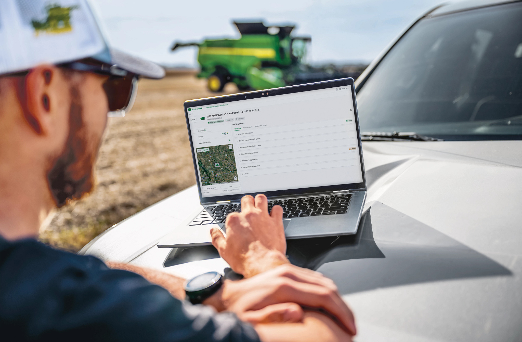 Farmer reviewing equipment information on a laptop beside a John Deere combine and draper