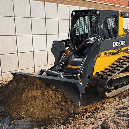 Front left view of a dozer blade pushing dirt on the front of a compact track loader