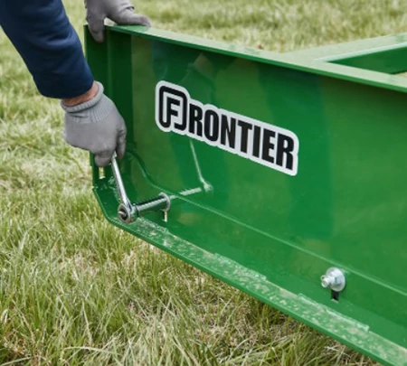 Gloved hand cranking open a bolt on the side of a green Frontier land plane with a wrench. The implement is sitting on grass.