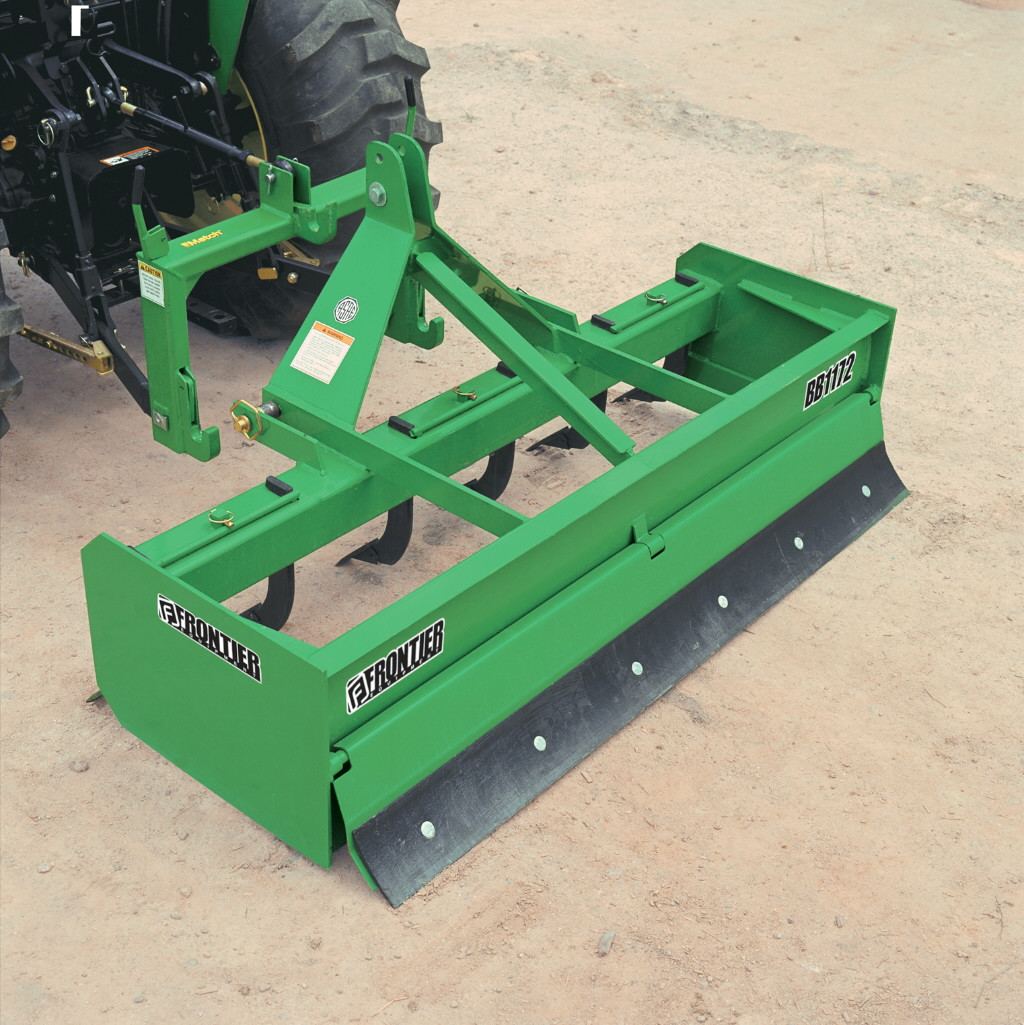 Rear view of Frontier BB1172 Box Blade attached to a tractor, showing the green frame, steel cutting edge, and floating tailgate resting on a dirt surface