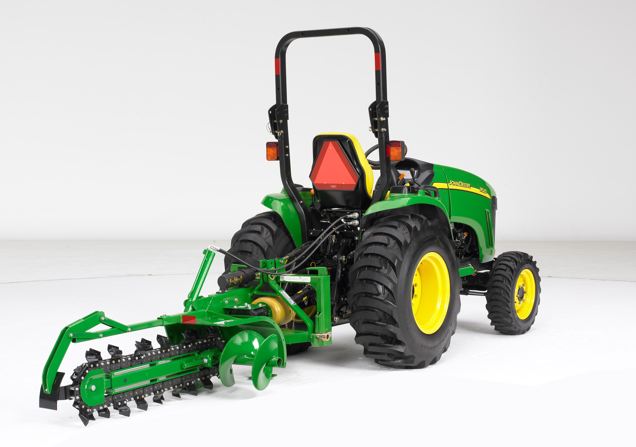 Rear view of a green tractor equipped with a mounted trenching attachment featuring a rotating chain and cutting teeth