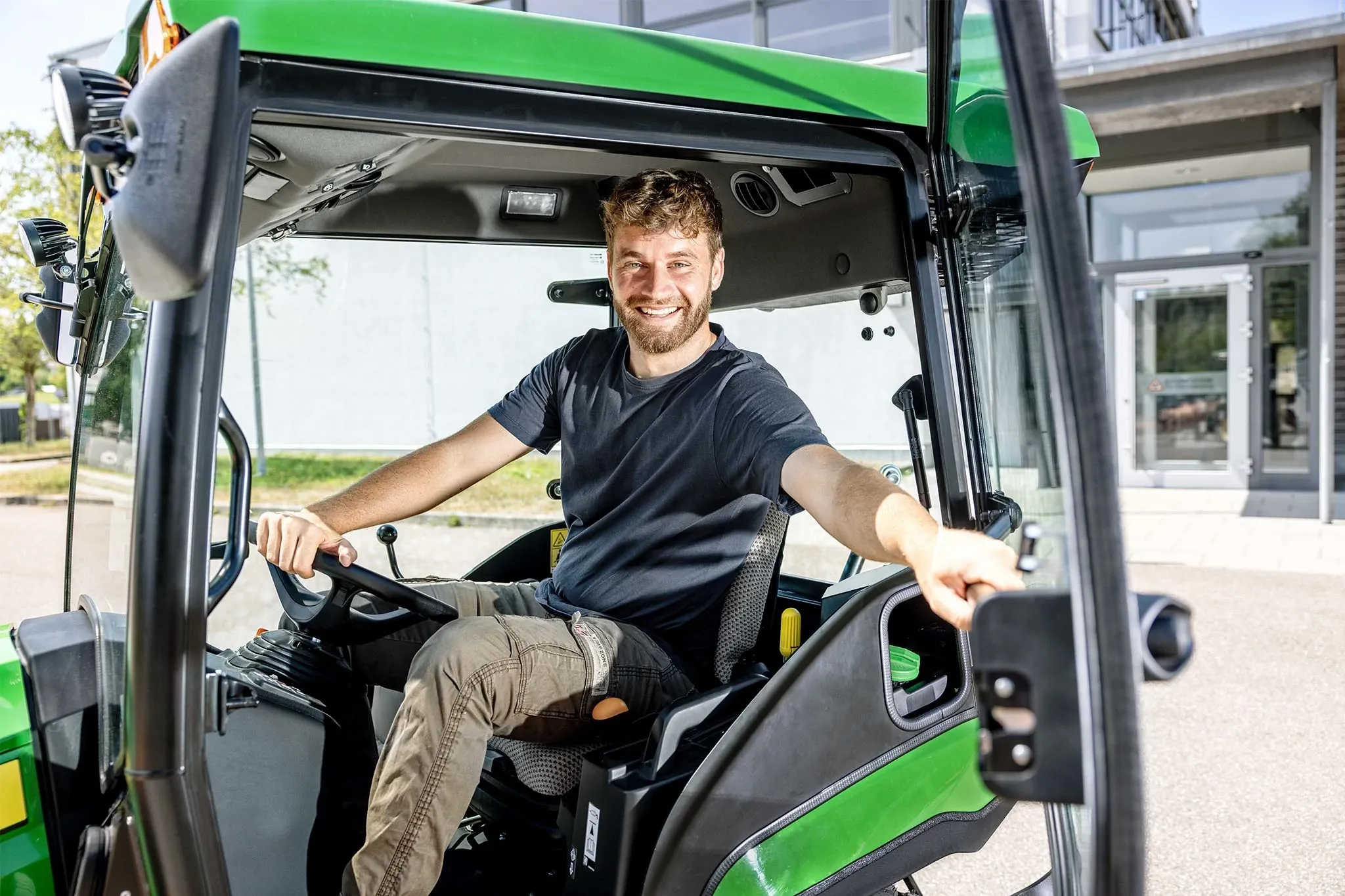 Operator seated inside a John Deere compact tractor cab with the door open