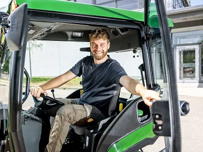 Operator seated inside a John Deere compact tractor cab with the door open