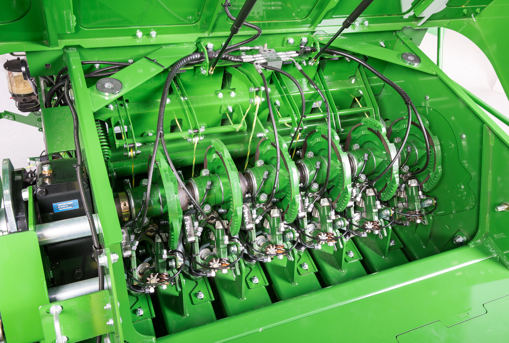 Close-up view of the double-tie knotter system of a baler, showing rotating shafts, linkages, springs, and hydraulic lines mounted in an open service compartment