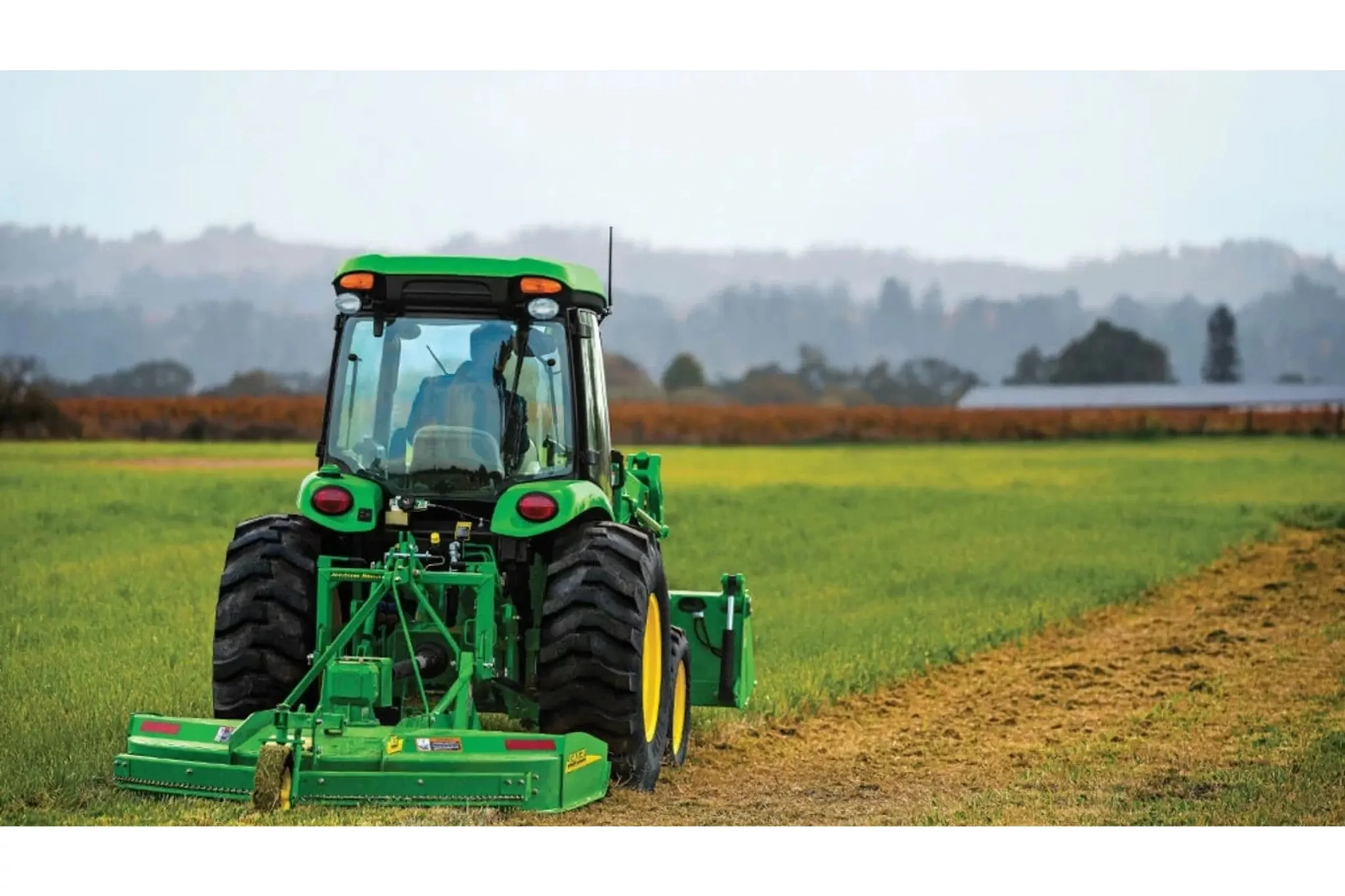 Farmer mowing a field with a 4052R Compact Tractor attachment