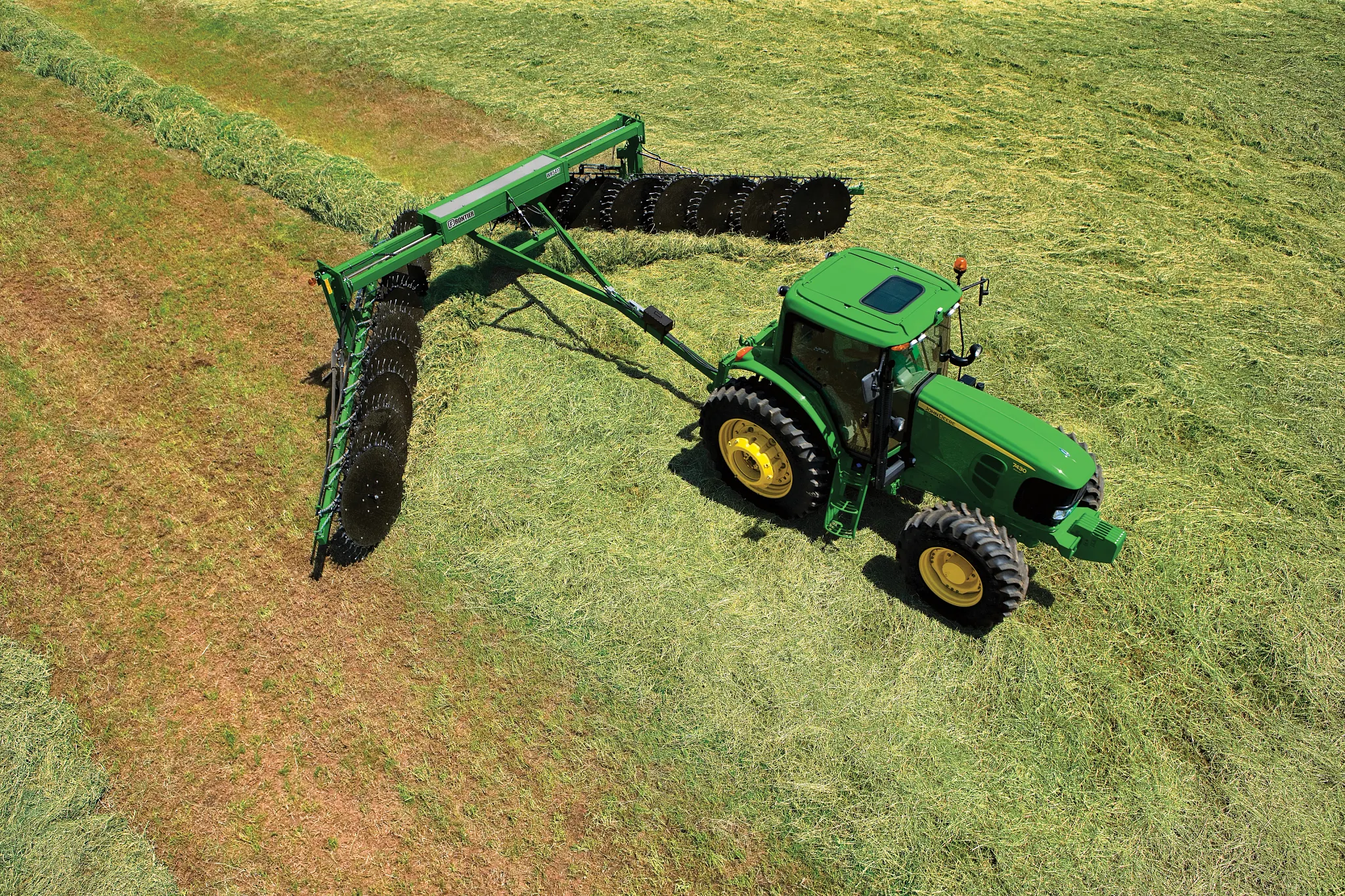 Top right view of a green tractor pulling a WR5417 wheel rake across a green hay field