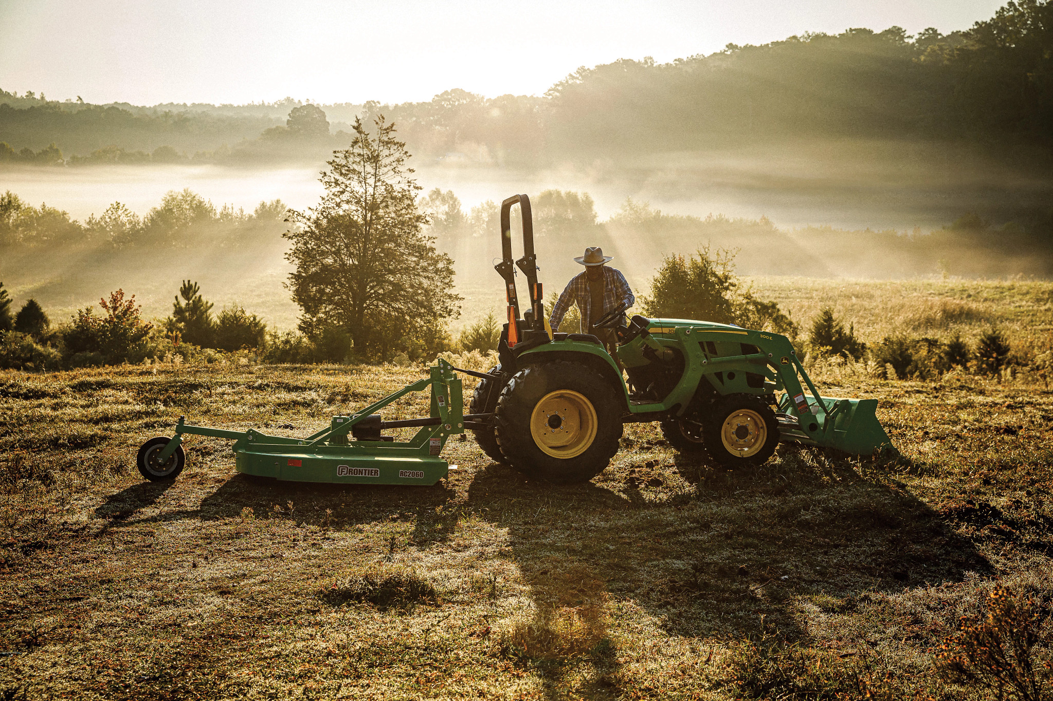 Man mows brush with John Deere 3032E Compact Tractor