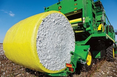 Front left close-up of a wrapped, round cotton bale on harvester in a field