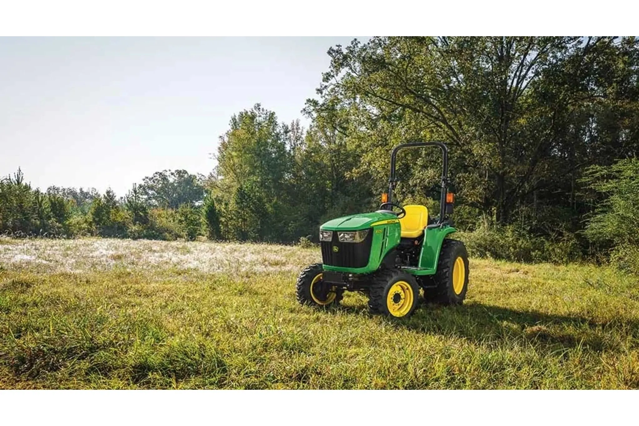 3025E 3 Series Compact Tractors with a green tractor parked in a field with trees in the background