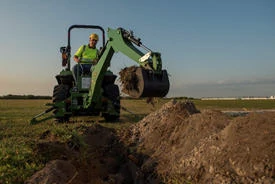 Front view of an operator in open station tractor using a 270B backhoe to dig a trench in a flat field at dusk