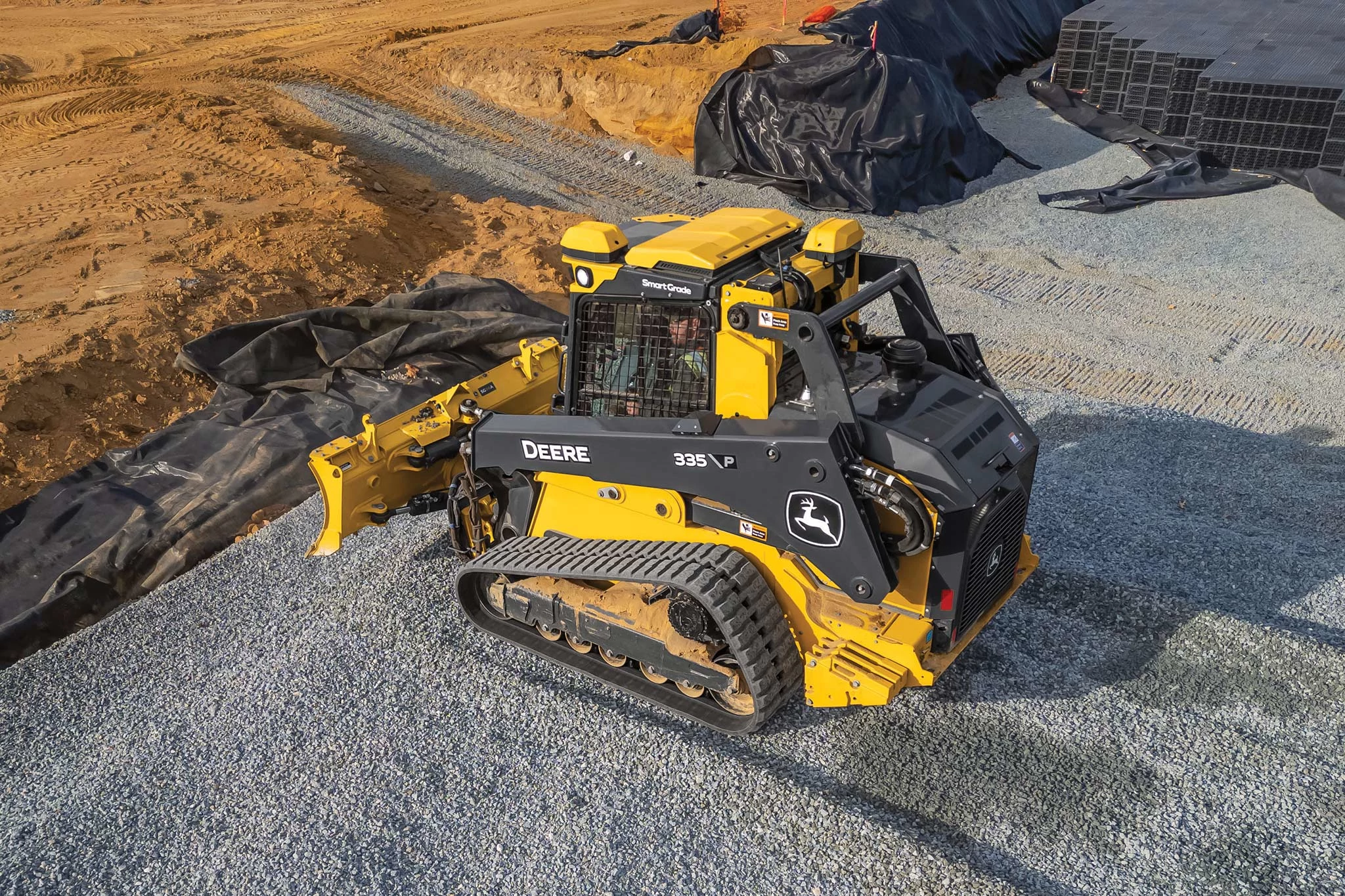 Side left aerial view of a yellow and black 335 P-Tier compact track loader on a gravel and dirt jobsite