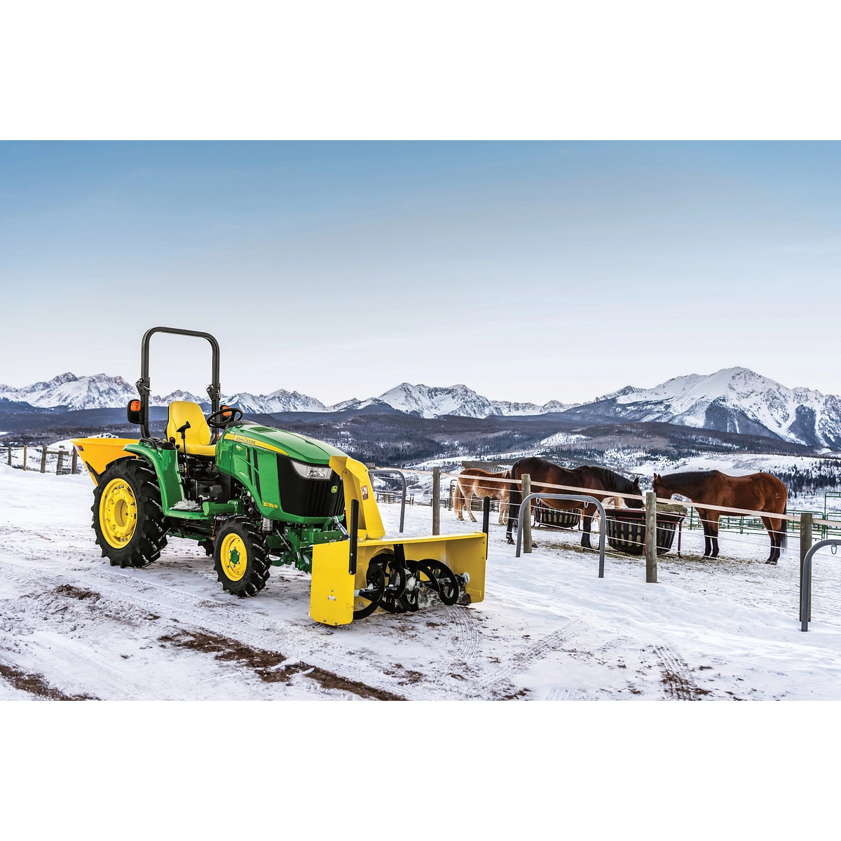 Front right view of an OOS 3039R compact utility tractor parked on a snowy road with horses and mountains in the background and yellow front-attached 60 inch snow blower Front right view of an OOS 3039R compact utility tractor parked on a snowy road with horses and mountains in the background and yellow front-attached 60 inch snow blower