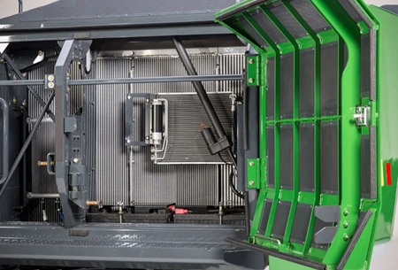 Open side panel of a forestry excavator showing an internal cooling system with radiator fins, hoses, wiring, and mounted components, with the hinged access door swung out