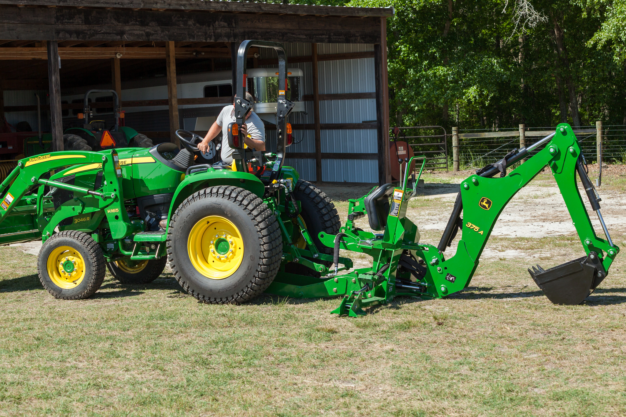 Left side view of a 3046R OOS tractor in grassy yard with operator managing H165 loader and 375A backhoe attachments